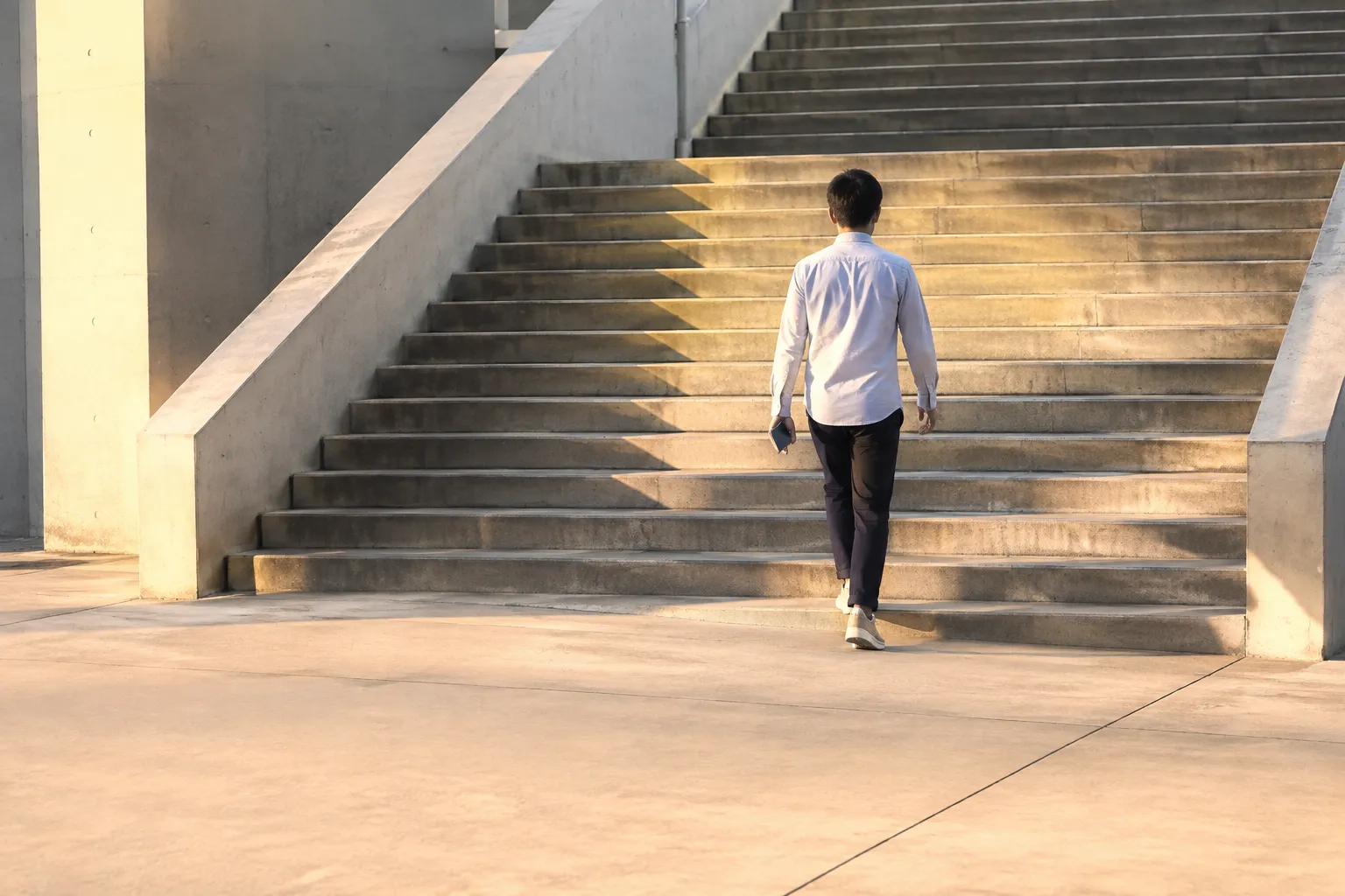 夕方の屋外の階段を、スマートフォンを持った人が上っていく後ろ姿